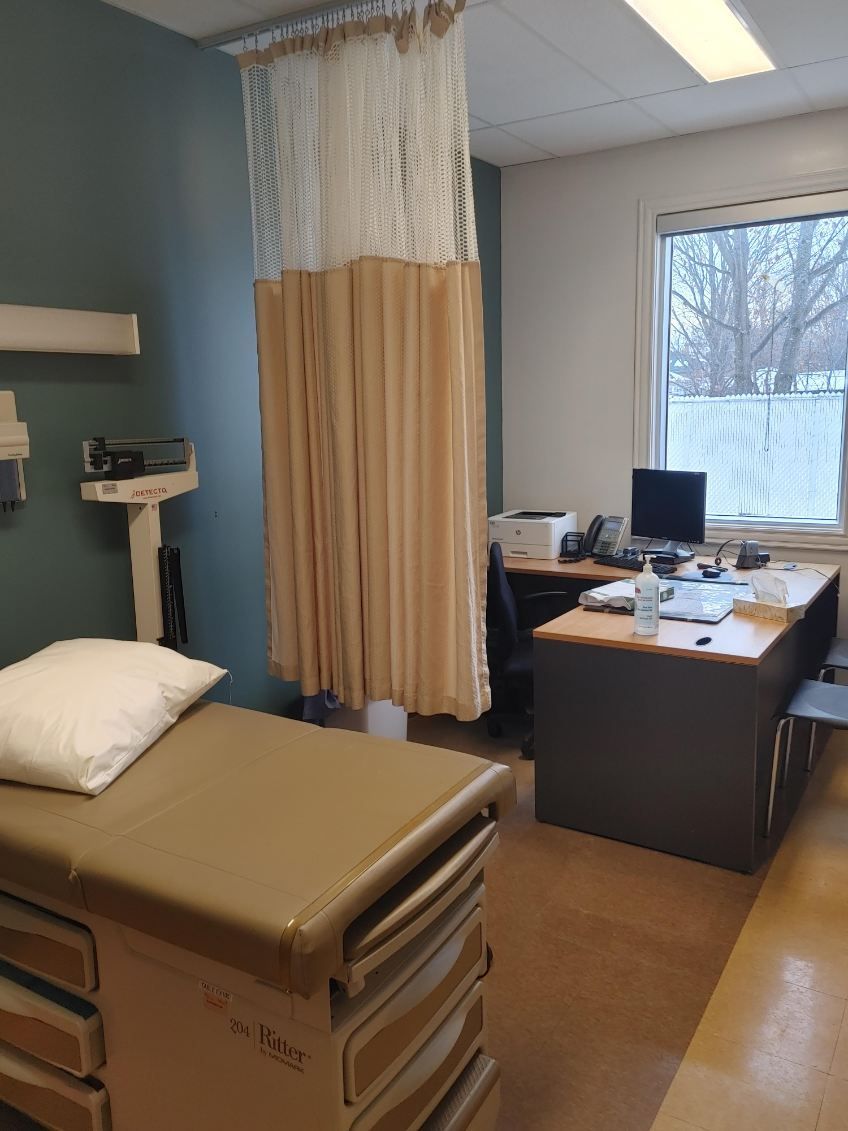 Salle d'examen du médecin avec table d'examen, bureau, rideau d'intimité et fenêtre.