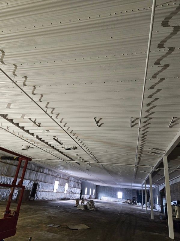 Vue intérieure d'un grand bâtiment inachevé avec un plafond métallique. Les travaux sont en cours.