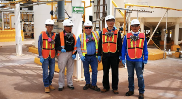 a group of men wearing hard hats and safety vests are posing for a picture .