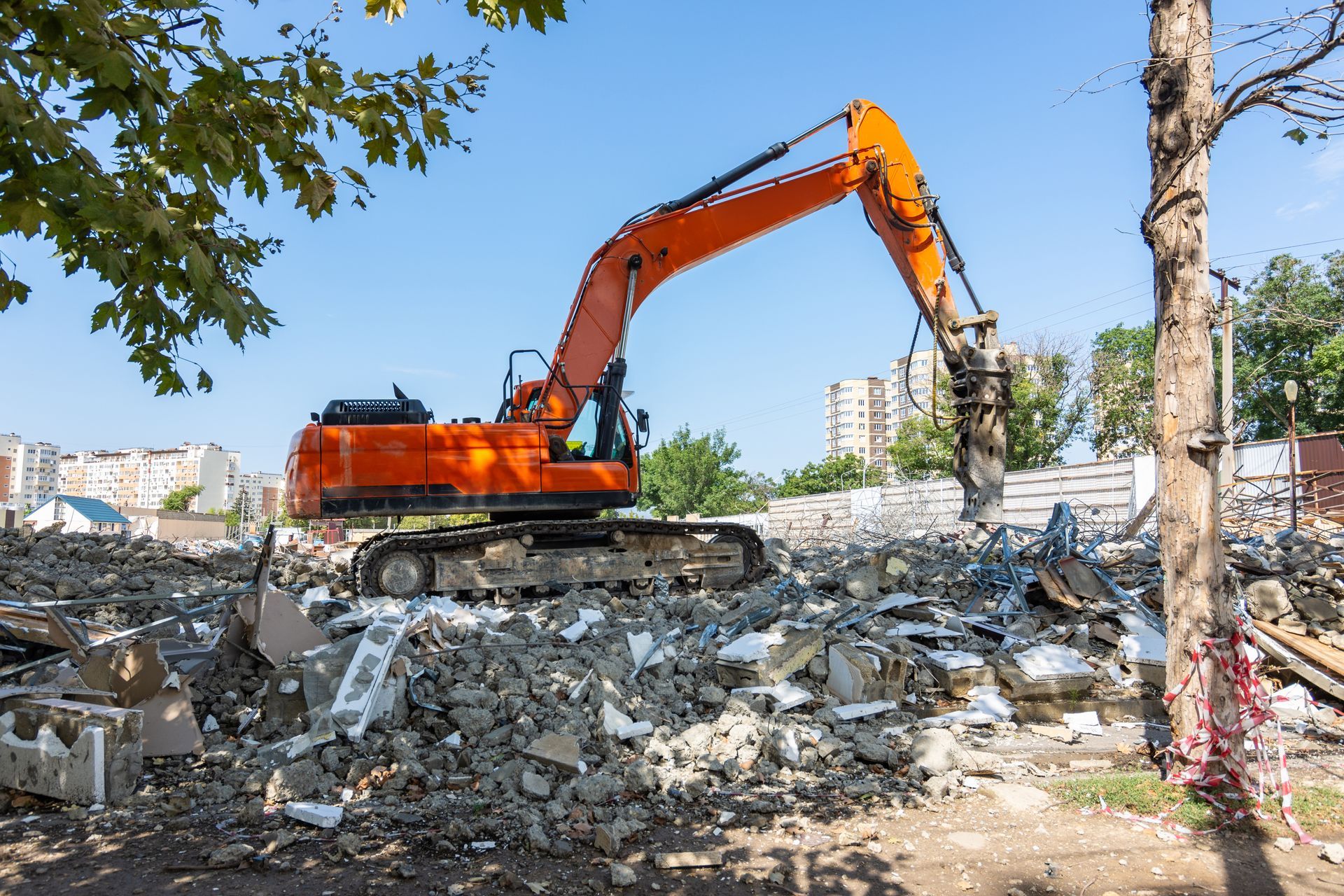 An orange excavator is demolishing a building on a construction site.