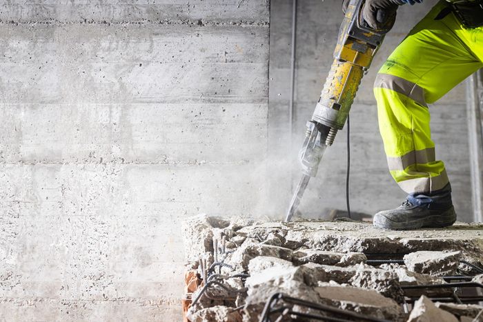 A construction worker is using a hammer to break a concrete wall.