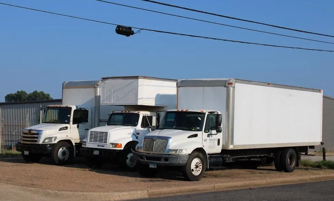 Three white trucks are parked next to each other on the side of the road.