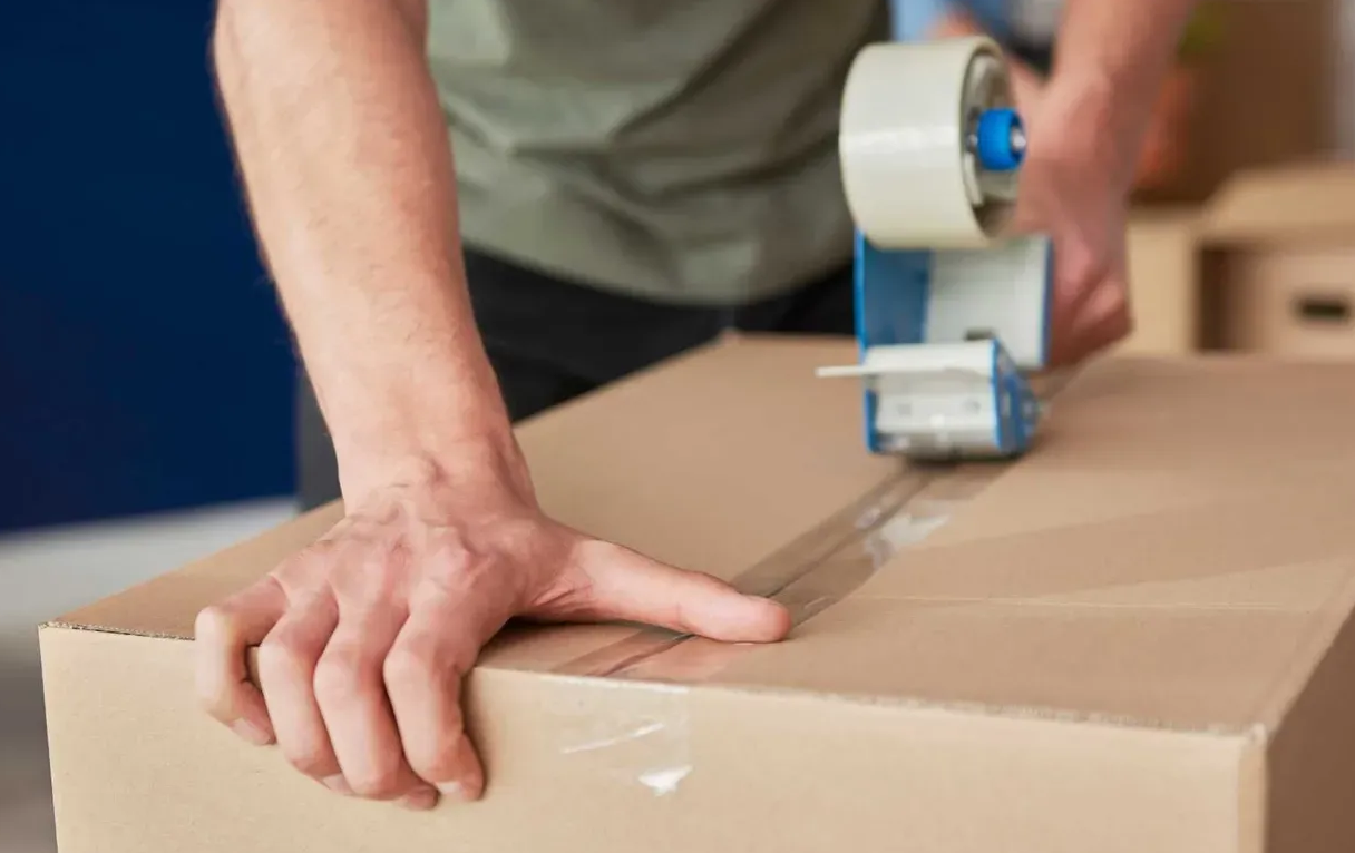 A person is taping a cardboard box with tape.