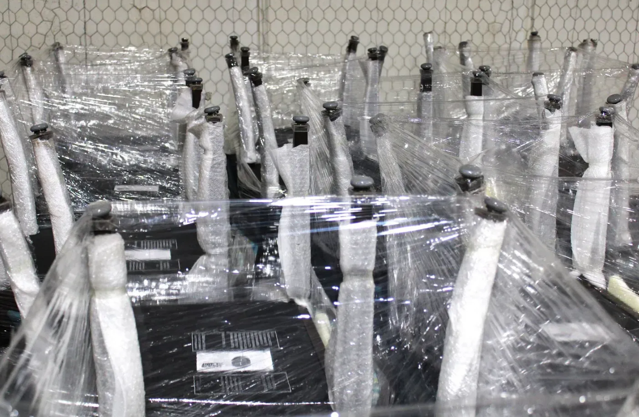 A bunch of chairs are wrapped in plastic in a warehouse