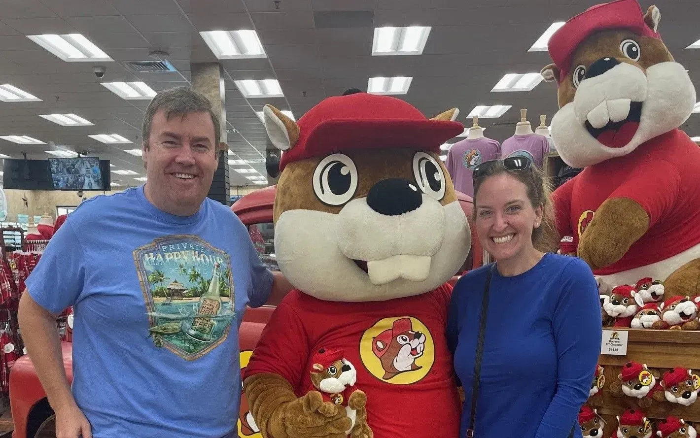 A man and a woman are standing next to a beaver mascot in a store.