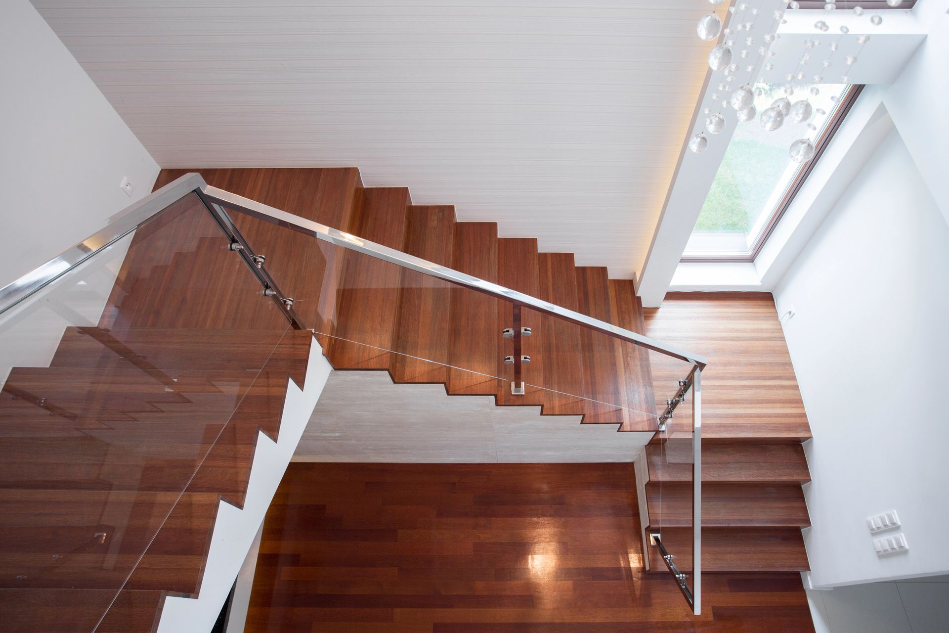 Una escalera de madera con barandilla de cristal y una ventana.