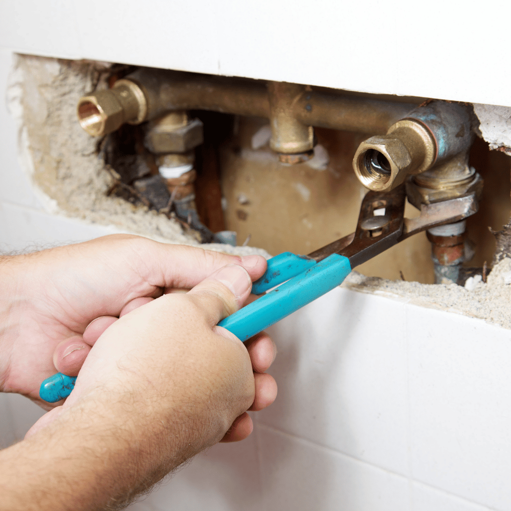 Hands using pliers to work on copper plumbing inside a wall.