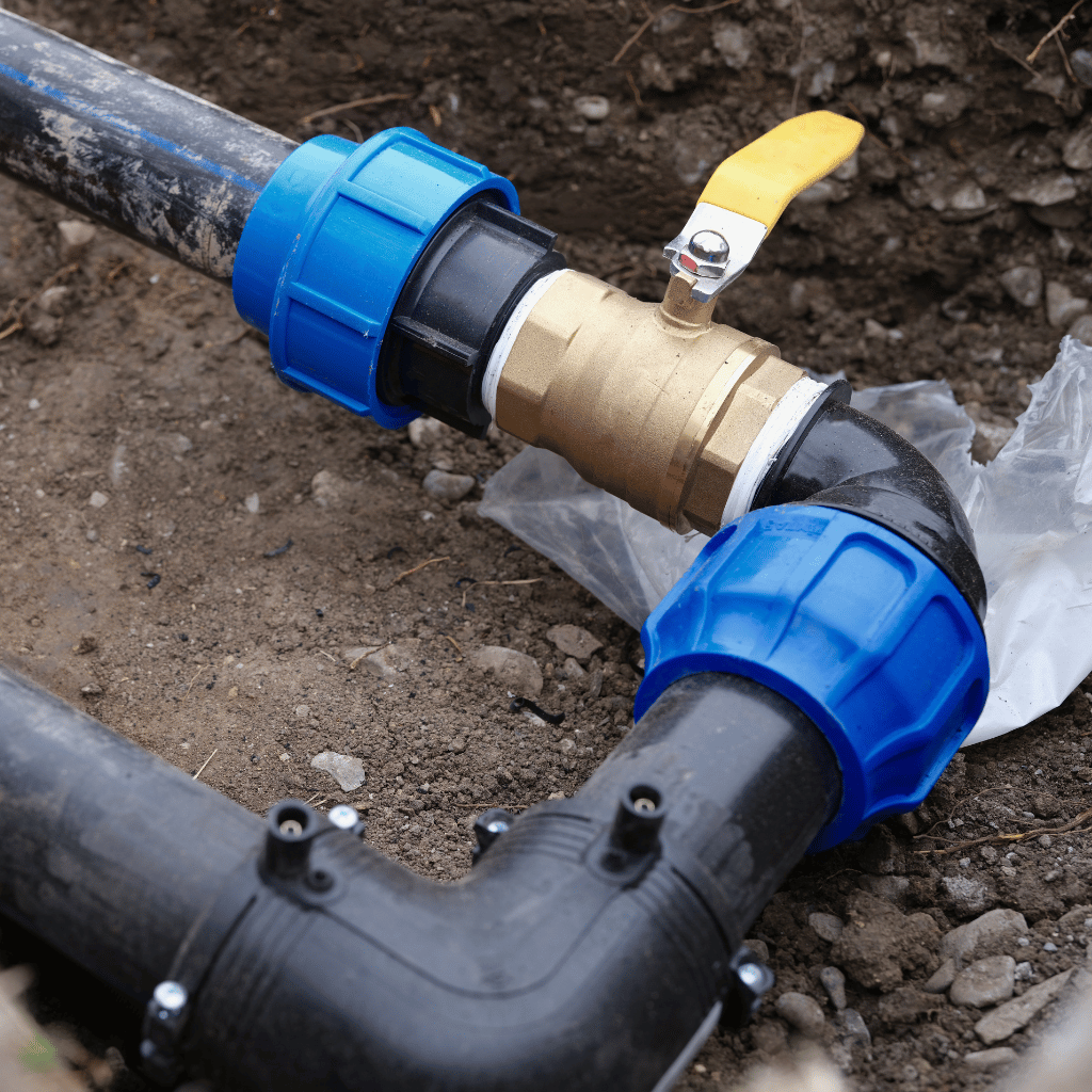 Black and blue pipes with a brass valve in a dirt trench.