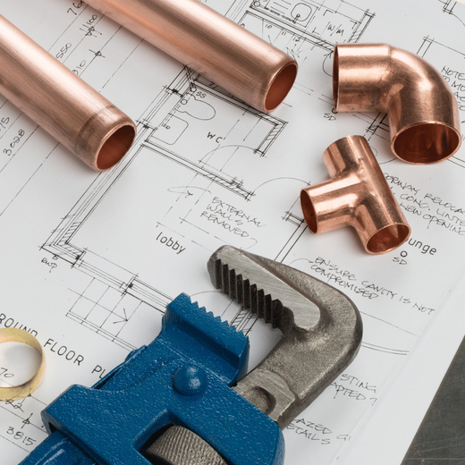 Copper pipes, elbow, and tee fittings with a wrench on a blueprint.