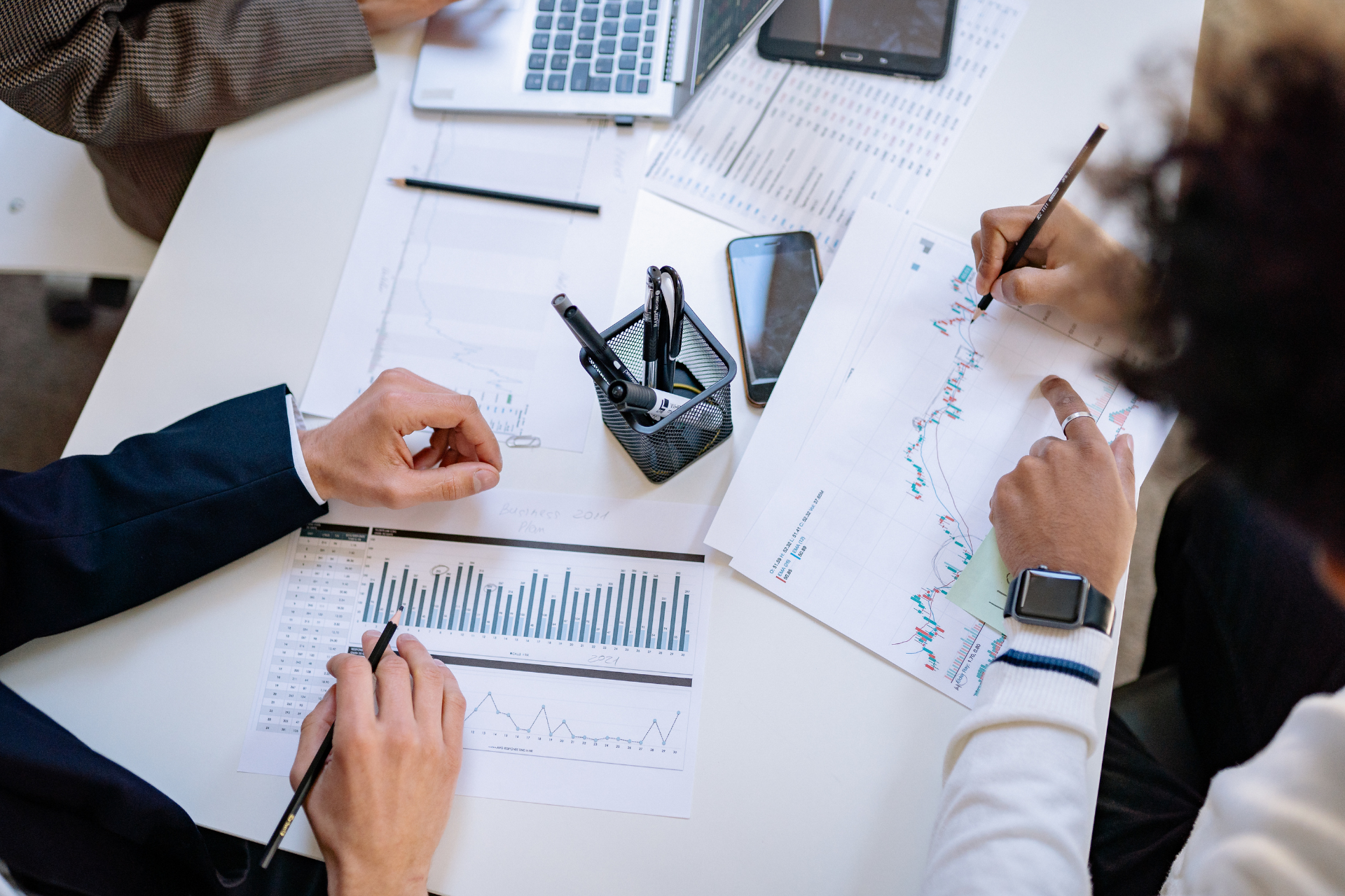 Three people sitting around a table collaborating while analyzing financial charts and documents.