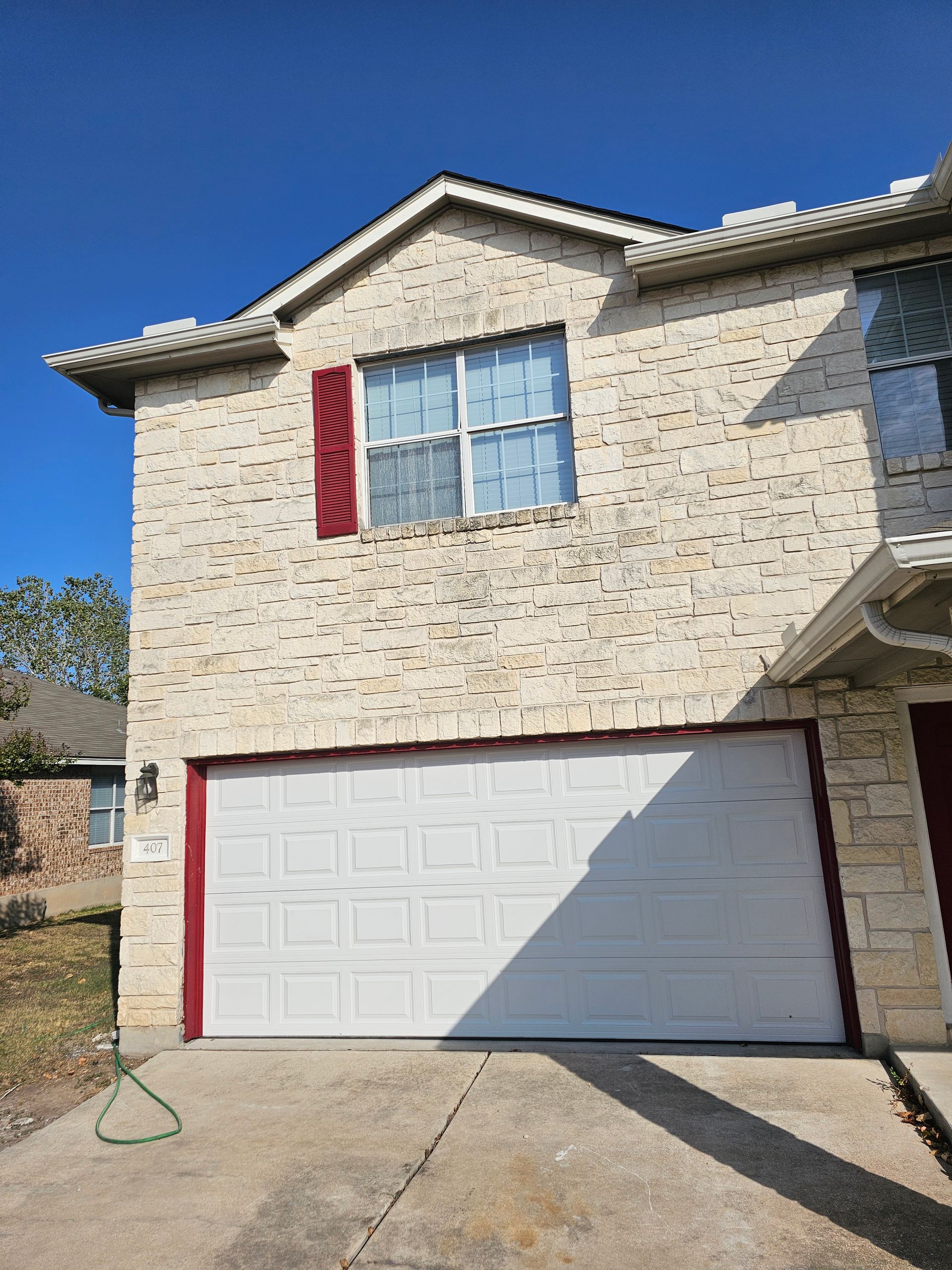 A brick house with a white garage door and red shutters.