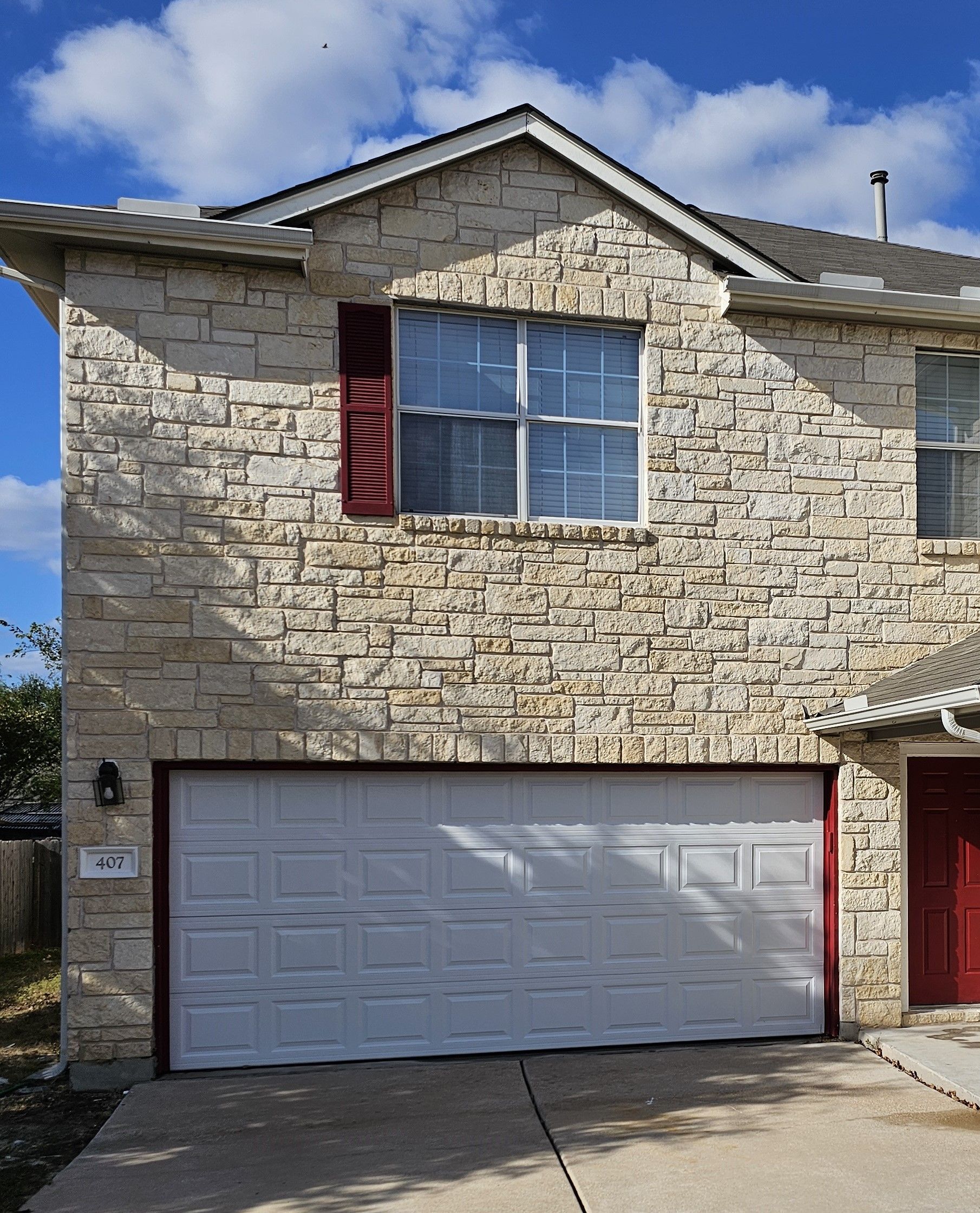 A brick house with a white garage door and a red door