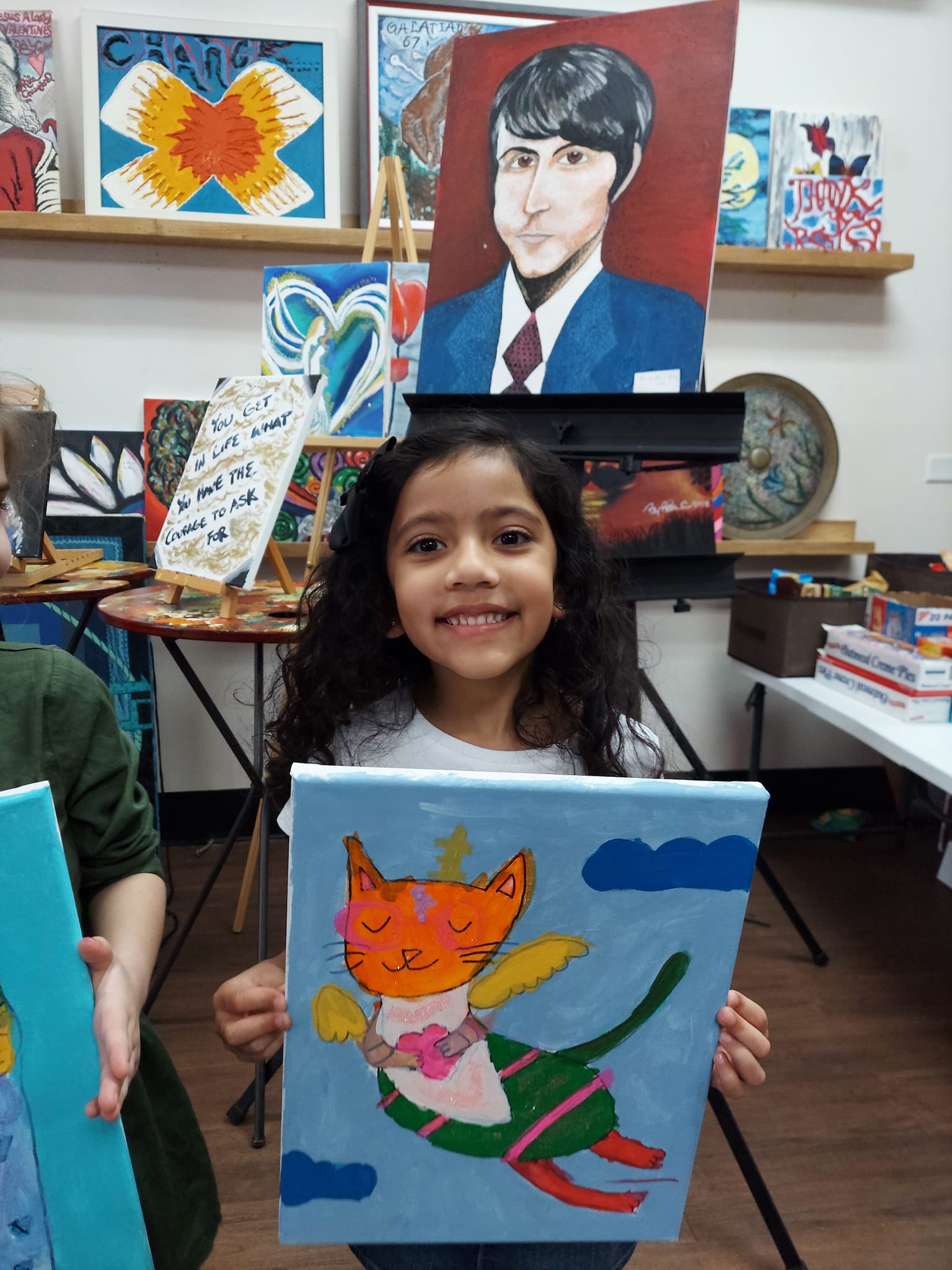 A young girl is holding a painting of a cat in a dress.
