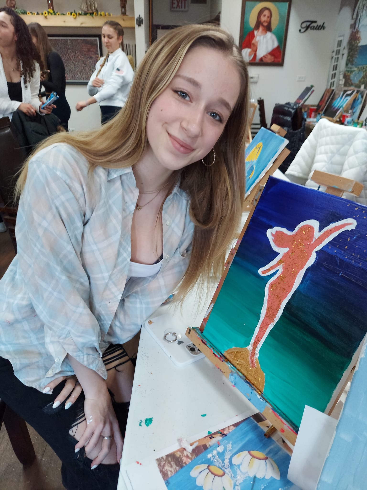 A woman is sitting at a table with a painting on it.