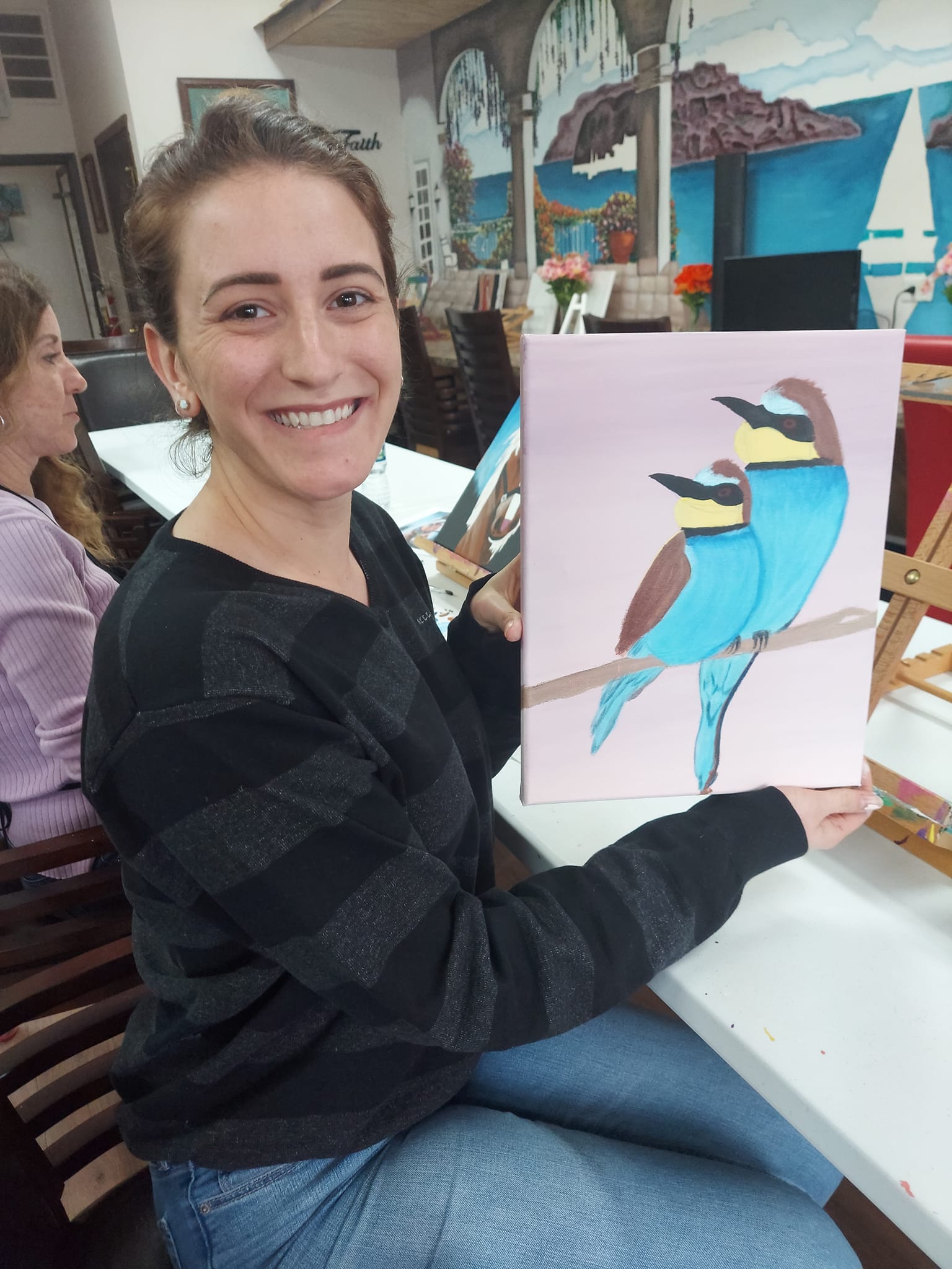 A woman is holding a painting of two birds on a branch.