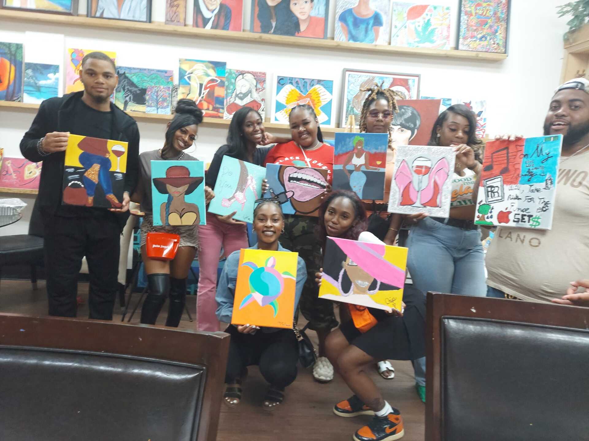 A group of people are posing for a picture with their paintings.