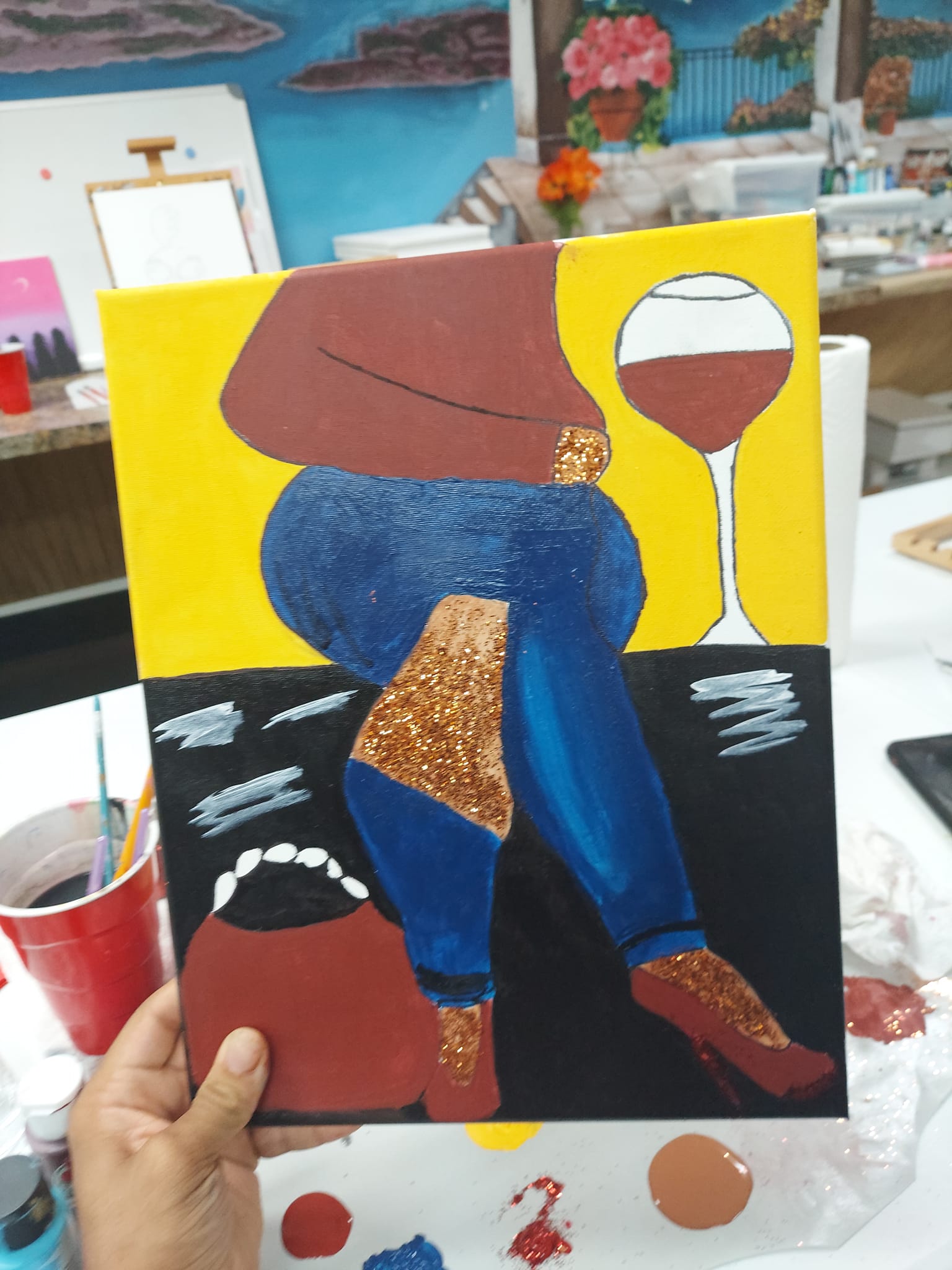 A person is holding a painting of a woman and a glass of wine