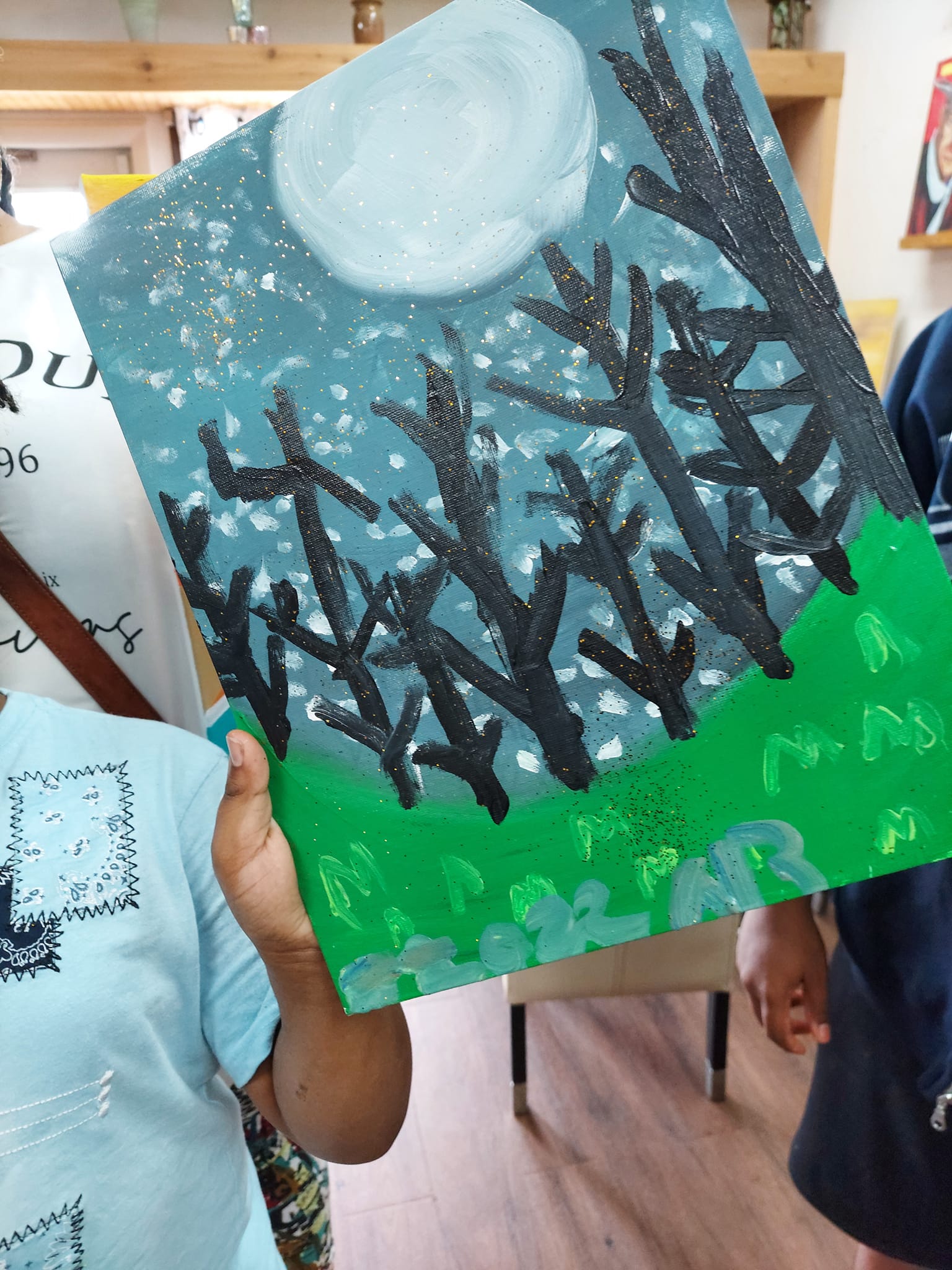 A child is holding up a painting of trees and a full moon