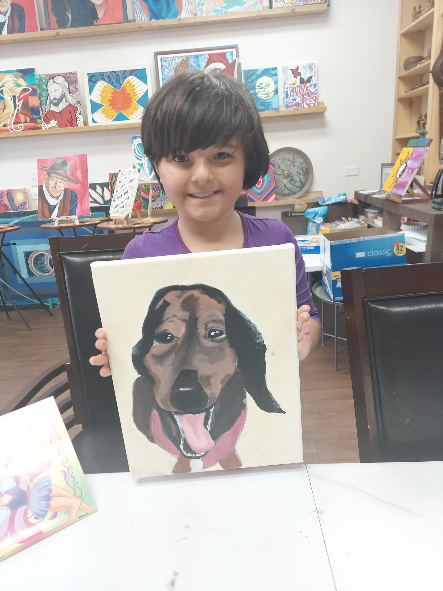 A young boy is holding a painting of a dog.
