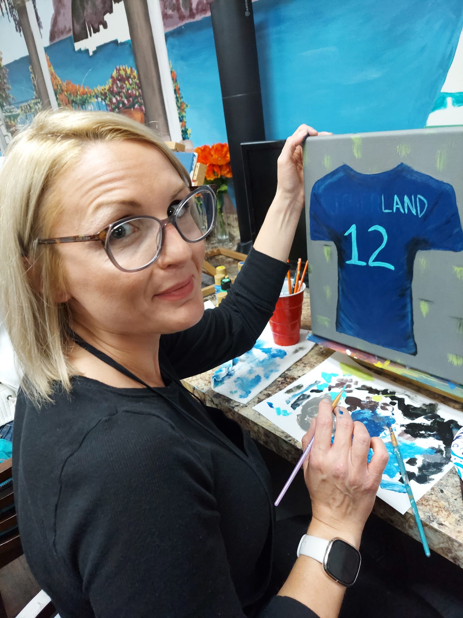 A woman is painting a shirt with the number 12 on it.