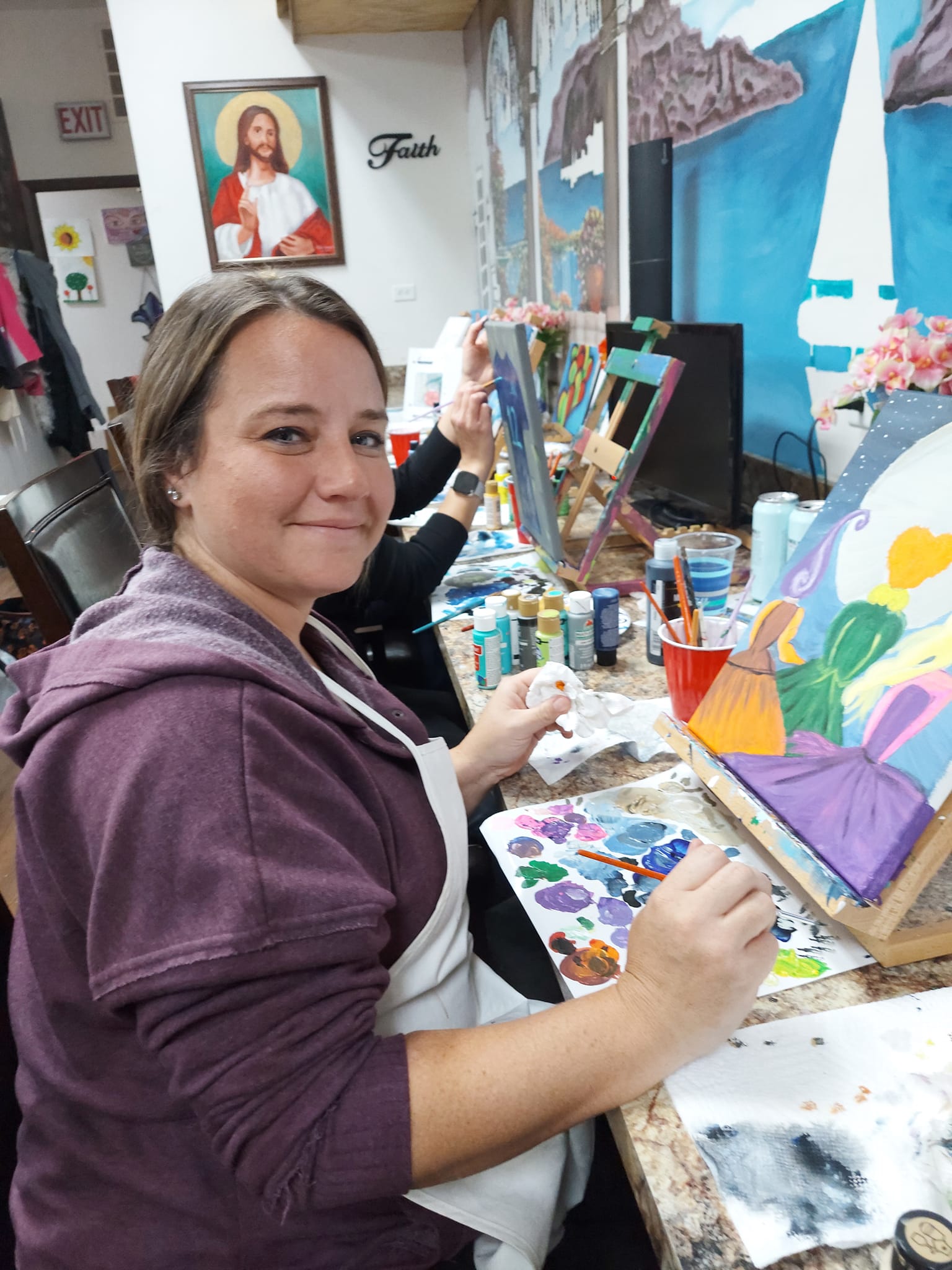 A woman is sitting at a table painting a picture.