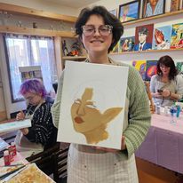 A woman is holding a painting of a woman 's face in a room.