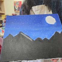 A woman is holding a painting of mountains at night with a full moon.
