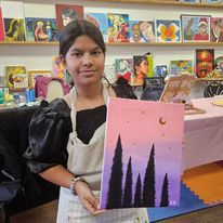 A young girl is holding a painting of trees in a room.
