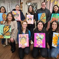 A group of people are posing for a picture while holding paintings.