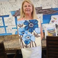 A woman is holding a painting of blue flowers in a vase.