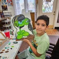 A young boy is holding a painting of a plant wearing headphones.
