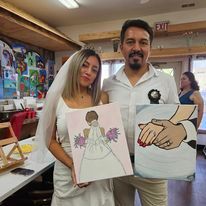 A man and a woman are holding a painting of a bride and groom holding hands.