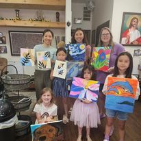 A group of young girls are holding up their paintings in a living room.