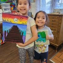 Two little girls are holding a painting of a bridge.