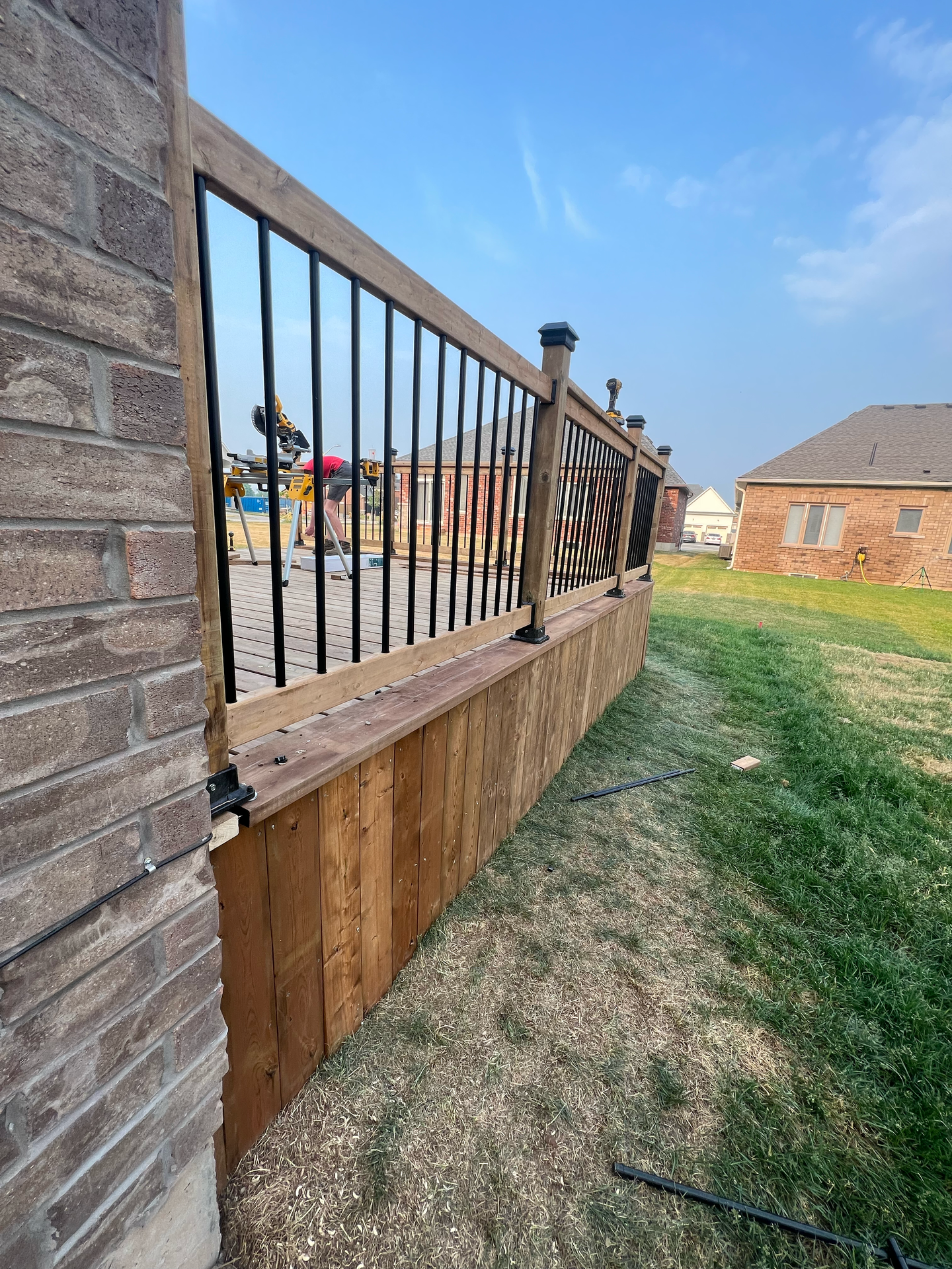 A wooden deck with a metal railing is sitting next to a brick wall.