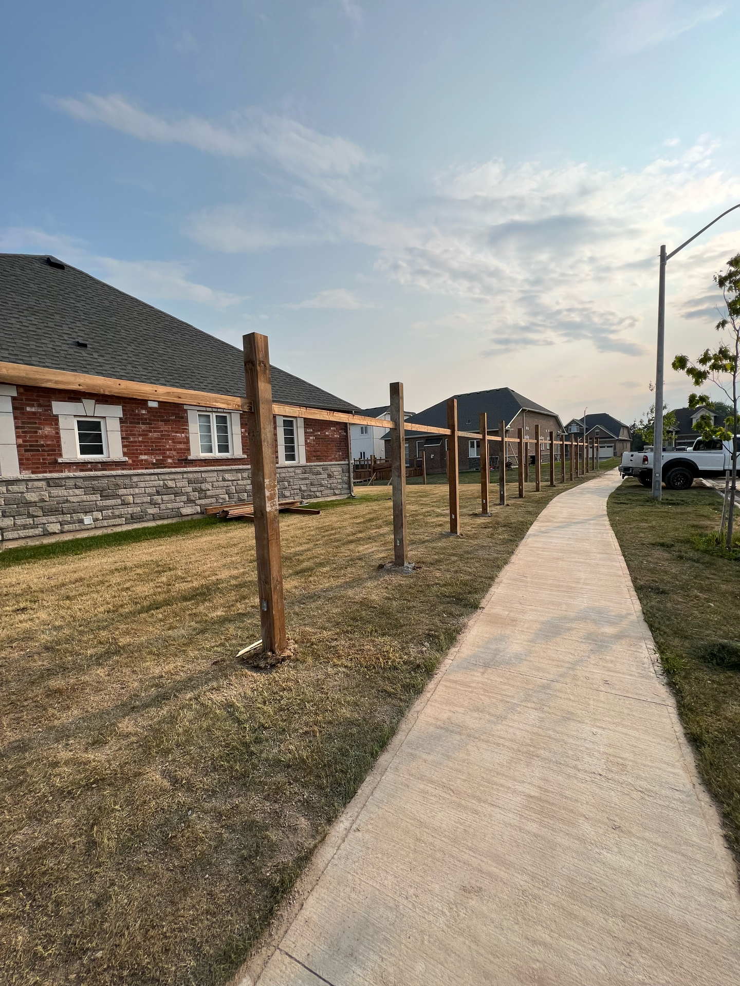 A wooden fence is being built next to a sidewalk in front of a house.