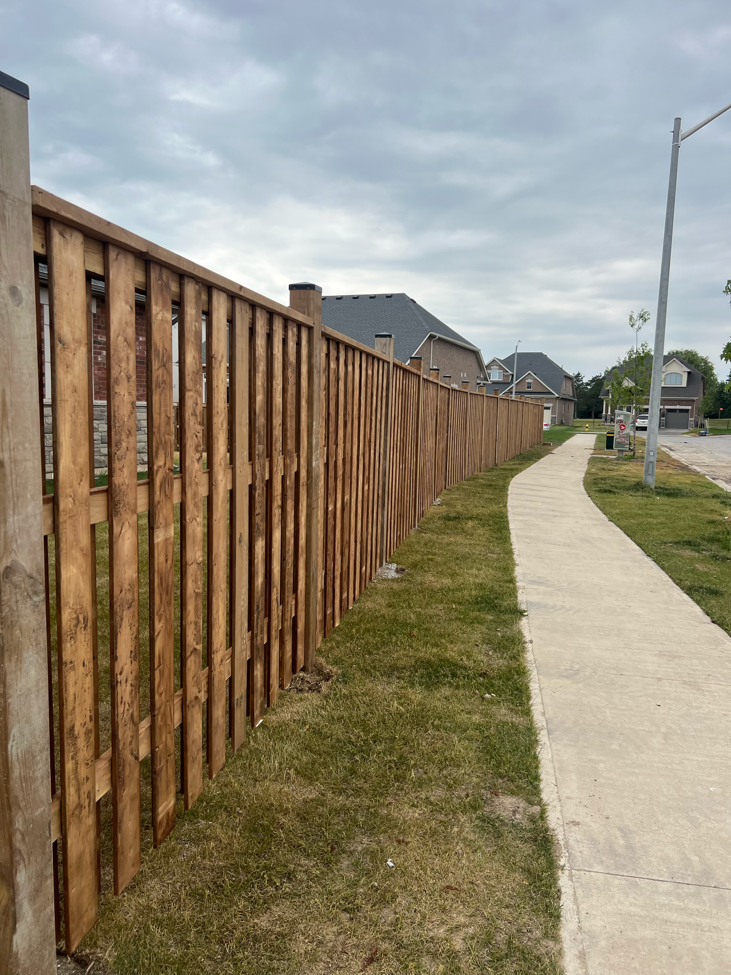 A wooden fence along a sidewalk in a residential area.