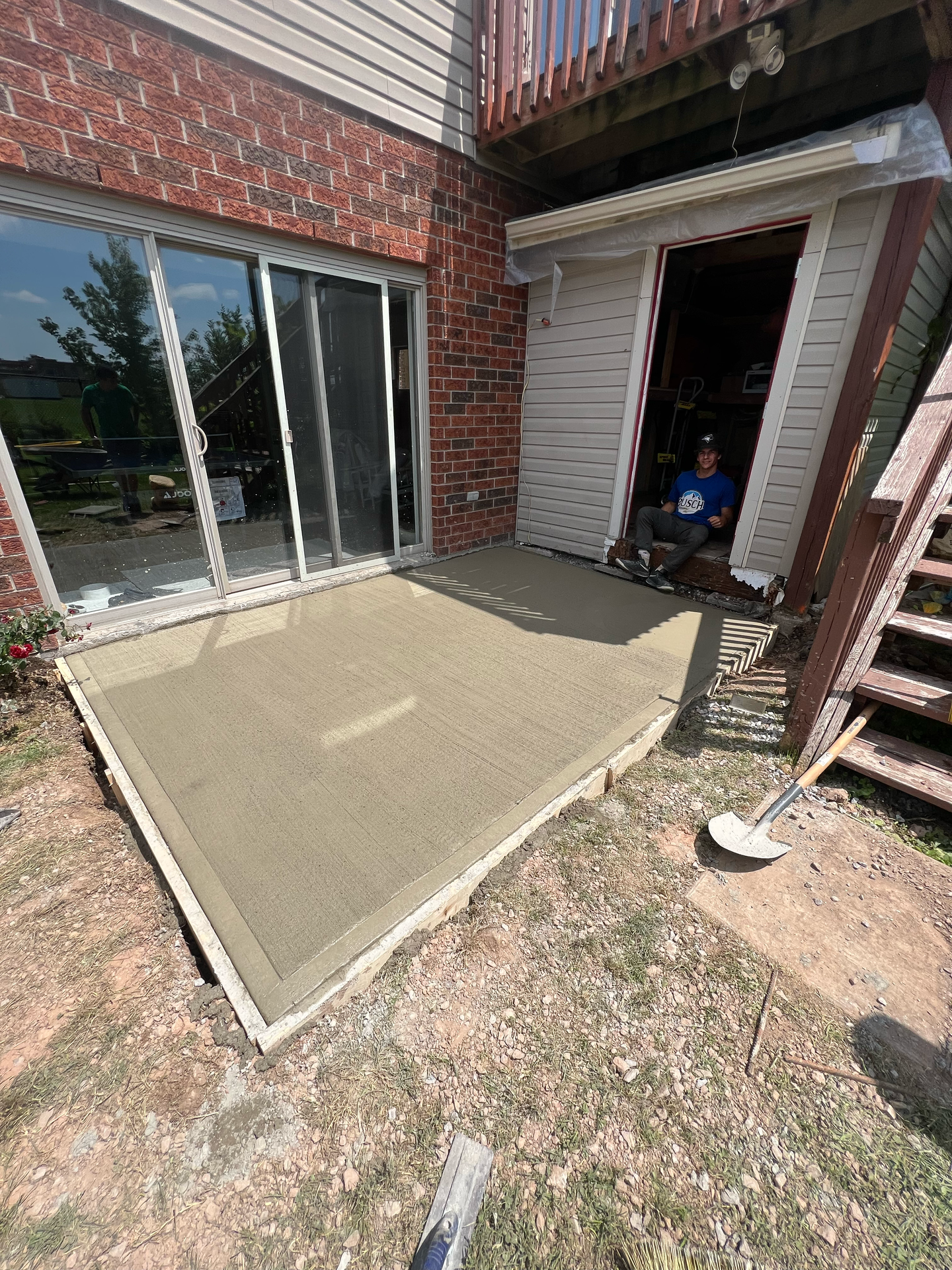 A man is sitting on a concrete patio in front of a house.