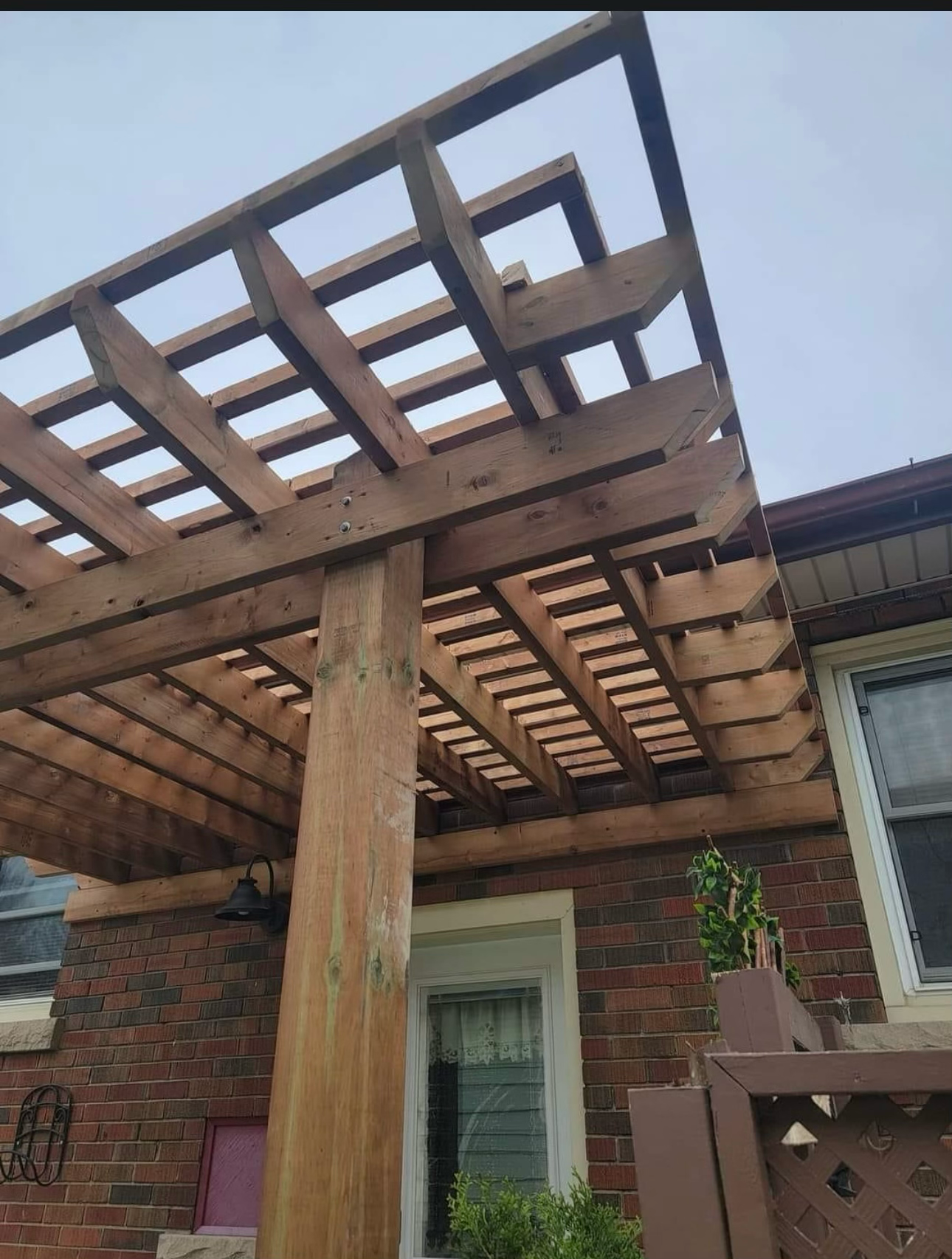 A wooden pergola is sitting on top of a brick house.