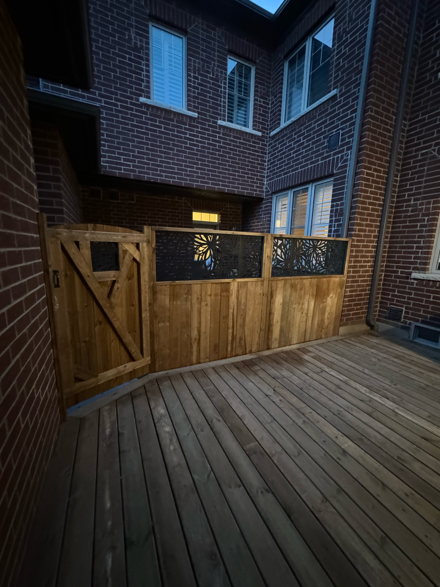 A wooden deck with a wooden fence and gate in front of a brick building.
