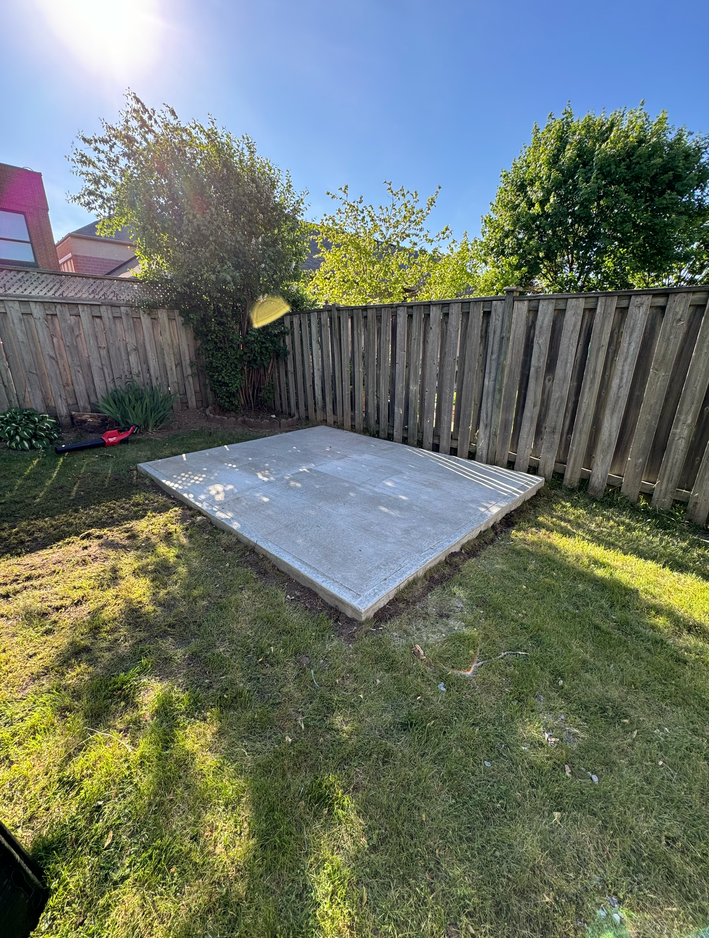 A concrete slab is sitting in the middle of a grassy yard next to a wooden fence.
