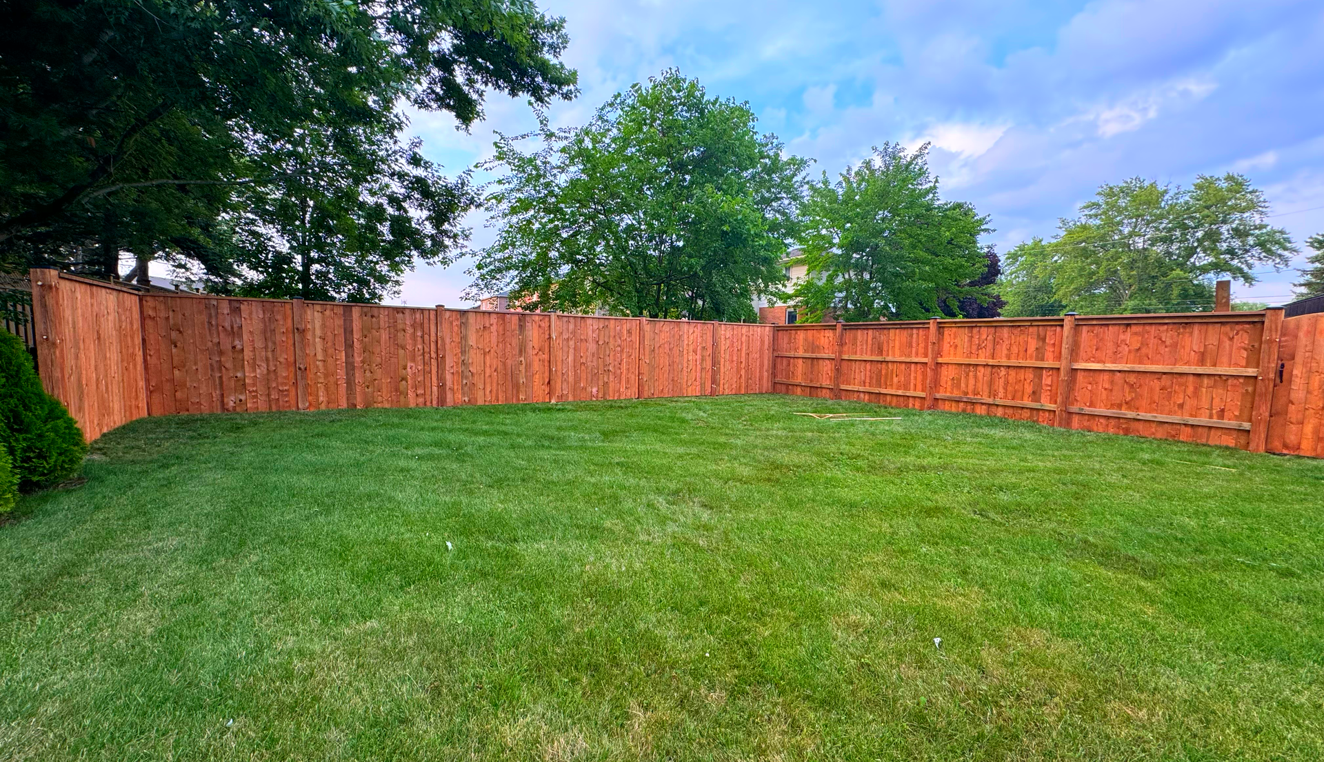 A wooden fence surrounds a lush green lawn in a backyard.