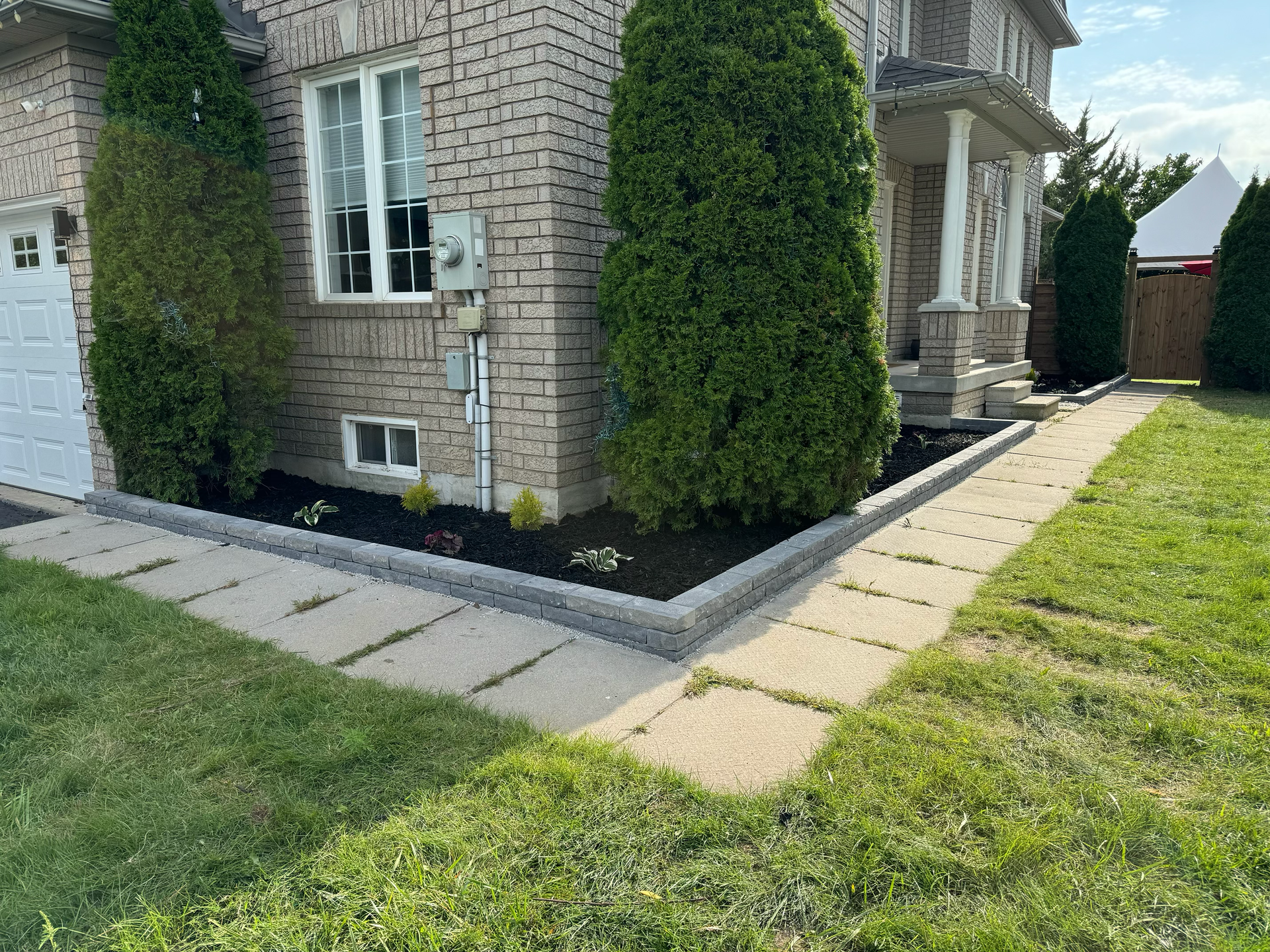 A brick house with a walkway leading to it and a lush green yard.