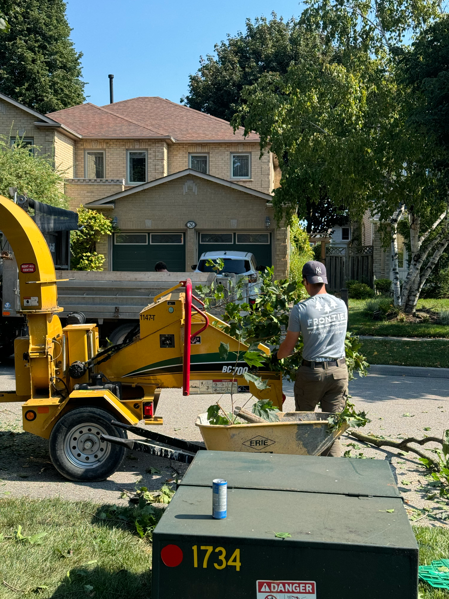 A man is standing next to a tree chipper in front of a house.