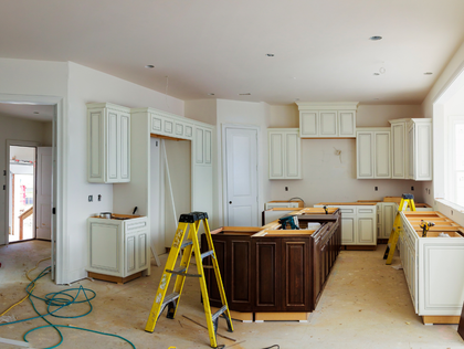 Unfinished kitchen with white cabinets, dark island, ladder, and tools scattered on the floor