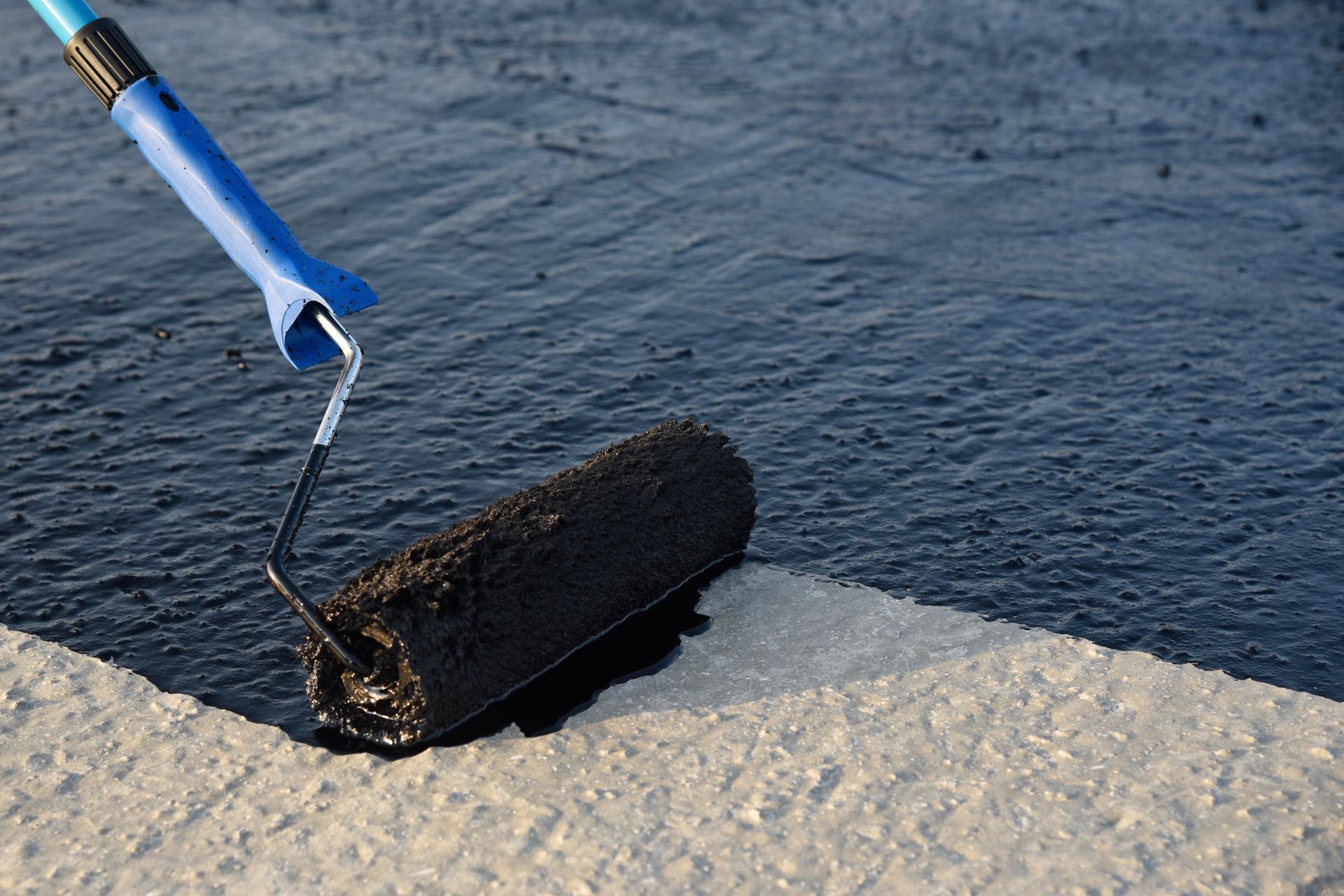 A blue-handled tool applying black sealant along a concrete edge by water A blue-handled tool applying black sealant along a concrete edge by water