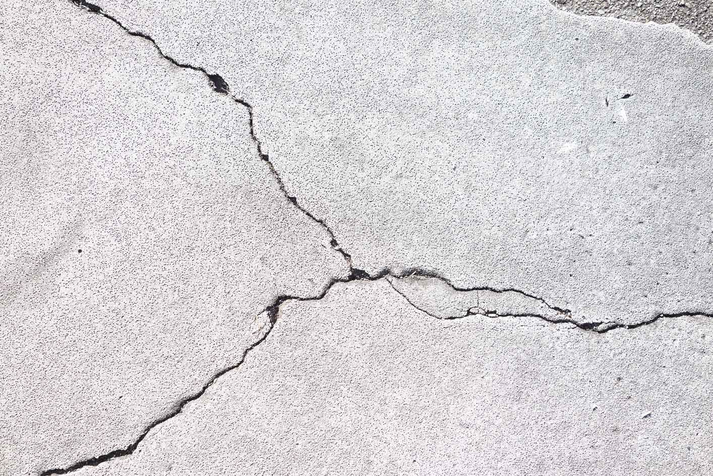 Close up of intersecting cracks on a light-colored concrete surface.