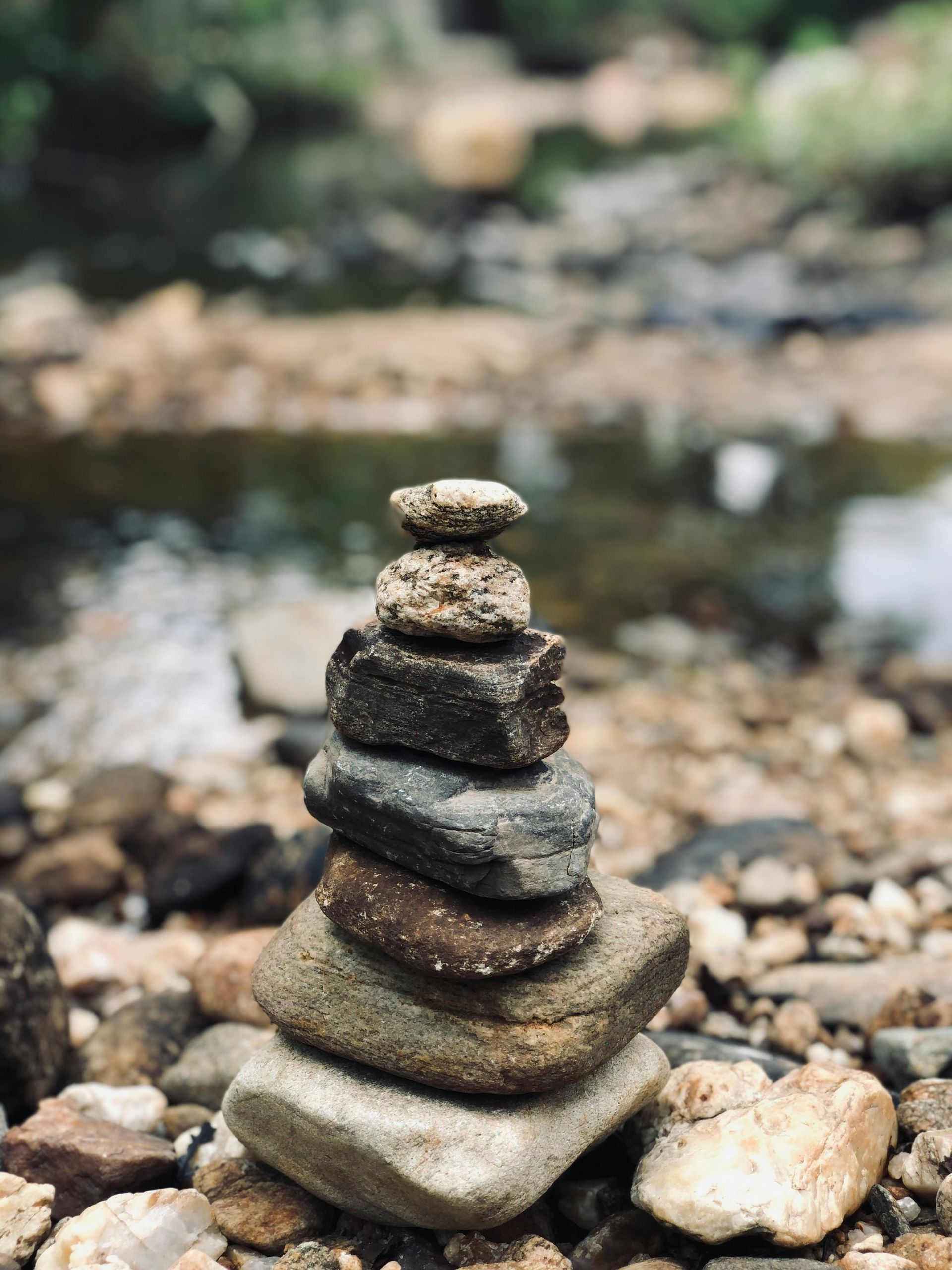 Stack of balanced stones in front of a blurred creek, brown and gray rocks.