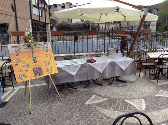 un buffet all'esterno sotto un ombrellone con dei piatti, bicchieri e fiori accanto a un tableau mariage 