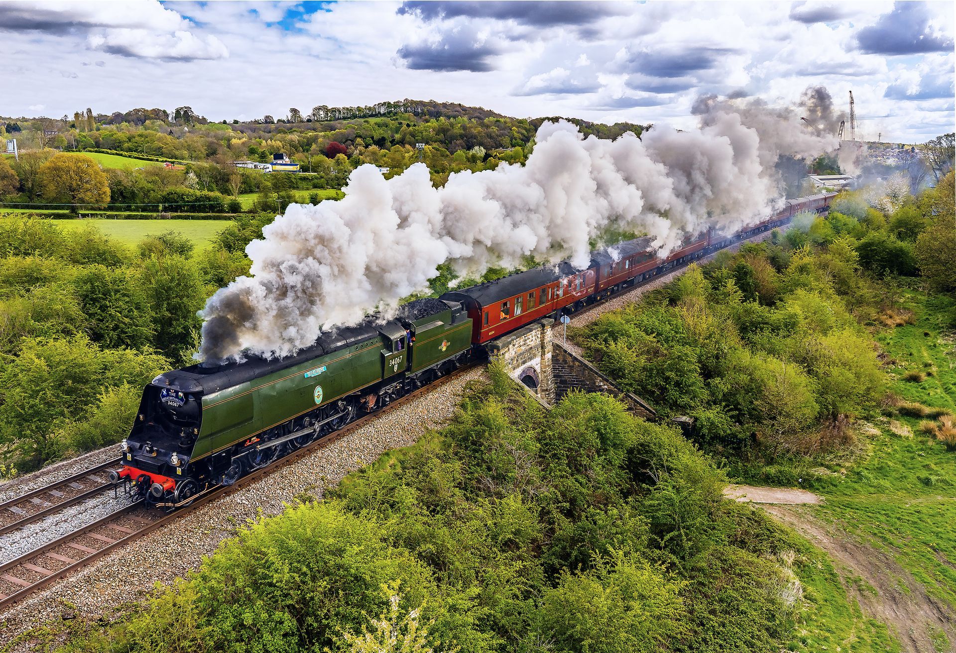 Steam train crossing a large stone viaduct over a town and river on a sunny day.